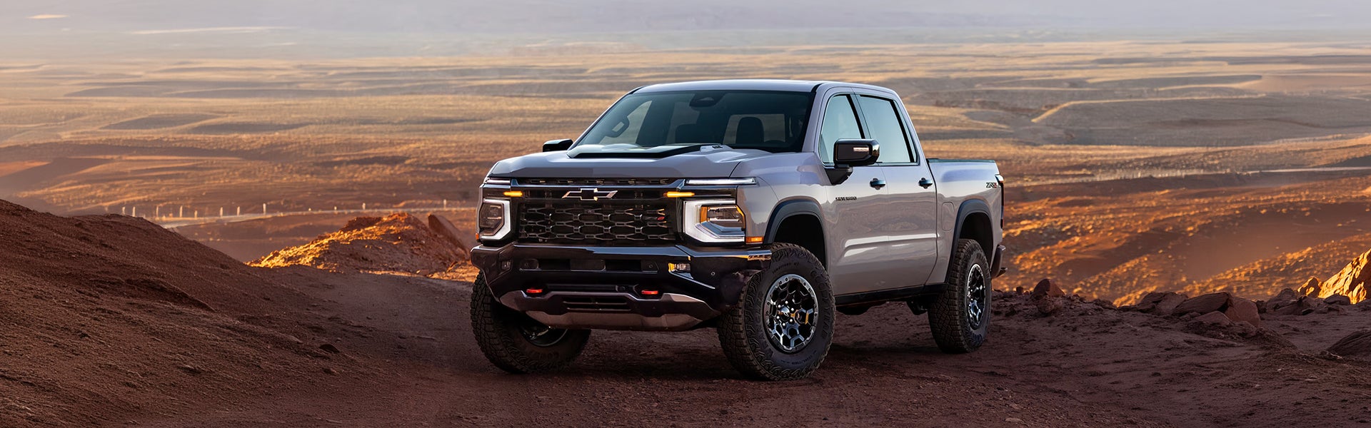 Silver 2027 Chevy Silverado 1500 parked on a desert ridge at sunset