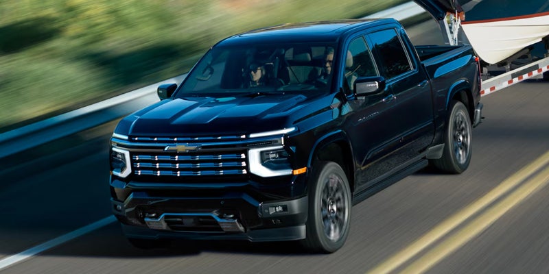 Black 2027 Chevy Silverado 1500 towing a boat on a highway