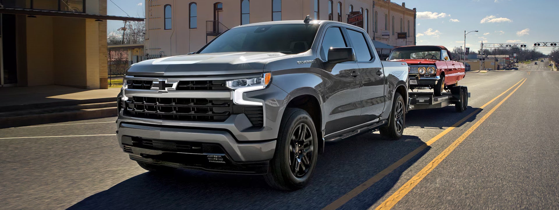 A grey Chevrolet Silverado 1500 pulling a classic red sports car on a trailer